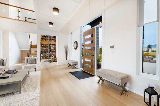 Bright modern entry hall with light wood floors, white walls, stairs, and a glass front door.