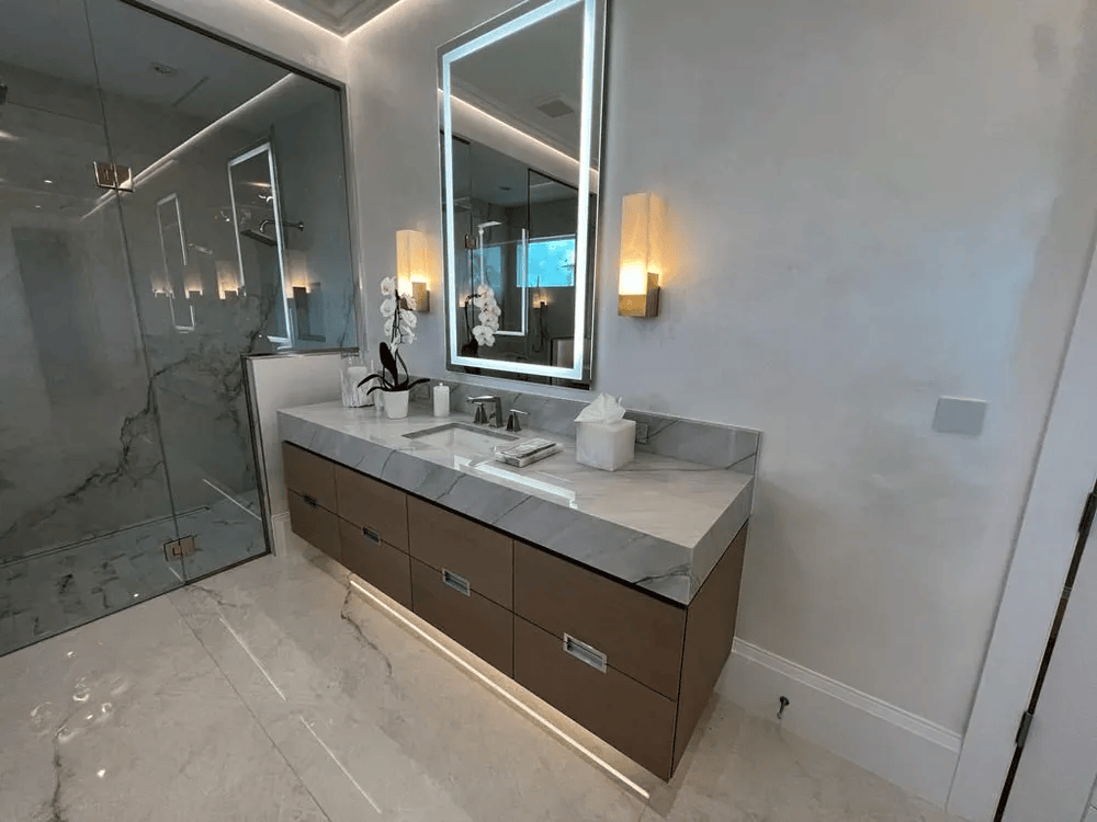 Modern bathroom vanity with double sinks, large mirror, marble walls, and a glass shower enclosure
