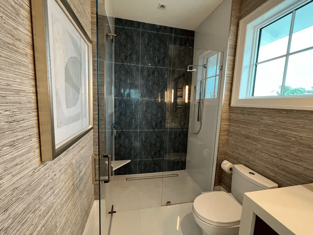 Modern bathroom with glass shower, dark tile wall, toilet, and window with blinds