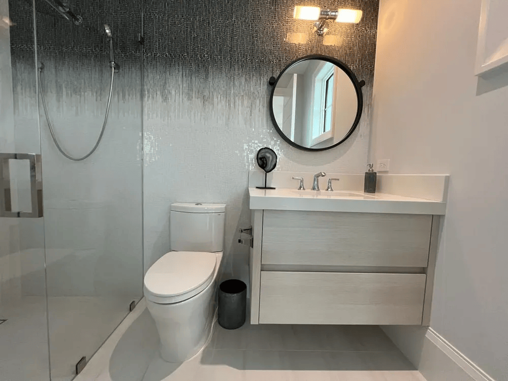 Modern bathroom with glass shower, toilet, floating vanity, round mirror, and white tile walls