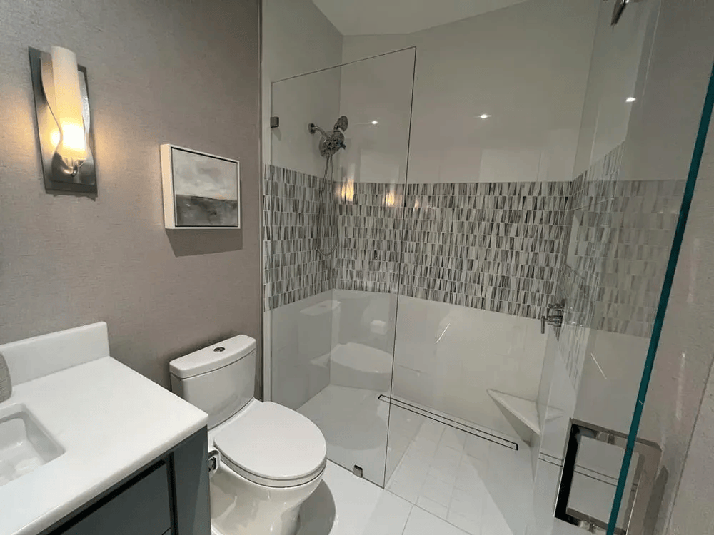 Modern bathroom with white toilet, vanity, and glass walk-in shower with gray tile accent wall