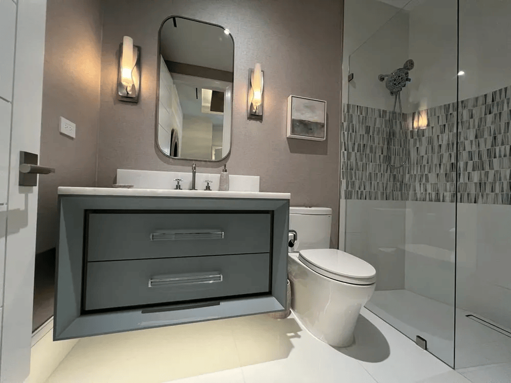 Modern bathroom with gray vanity, mirror, wall sconces, toilet, and glass-enclosed shower