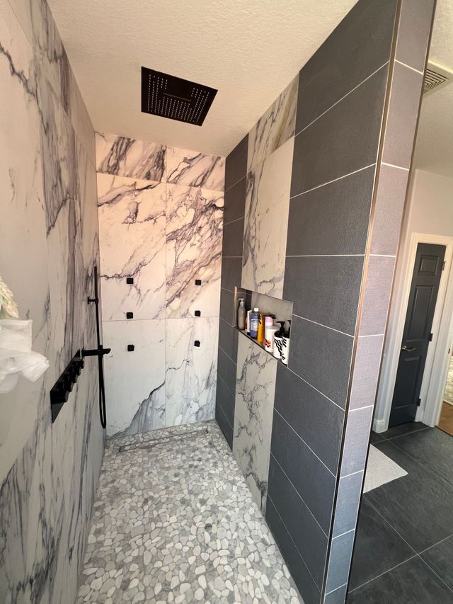 Modern bathroom shower with gray tile, marble walls, and pebble floor