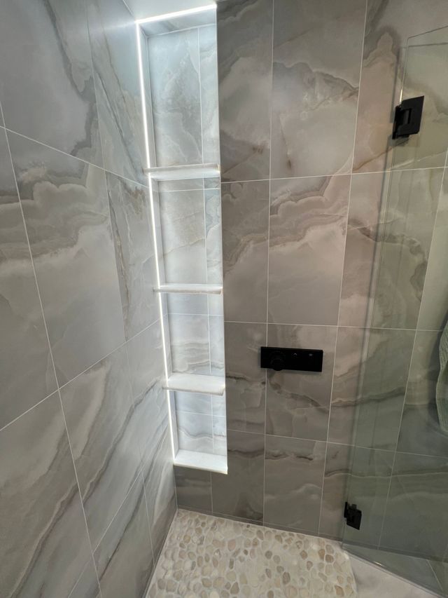 Modern tiled shower with glass partition, built-in niche, and floor drain.