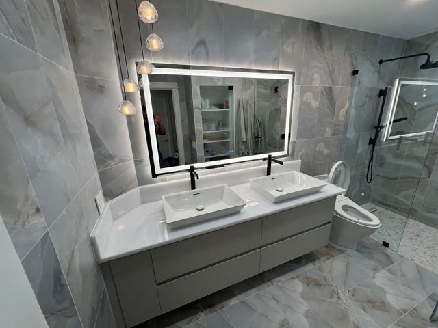 Modern bathroom with double vanity, large mirror, white sinks, and gray tiled walls and floor