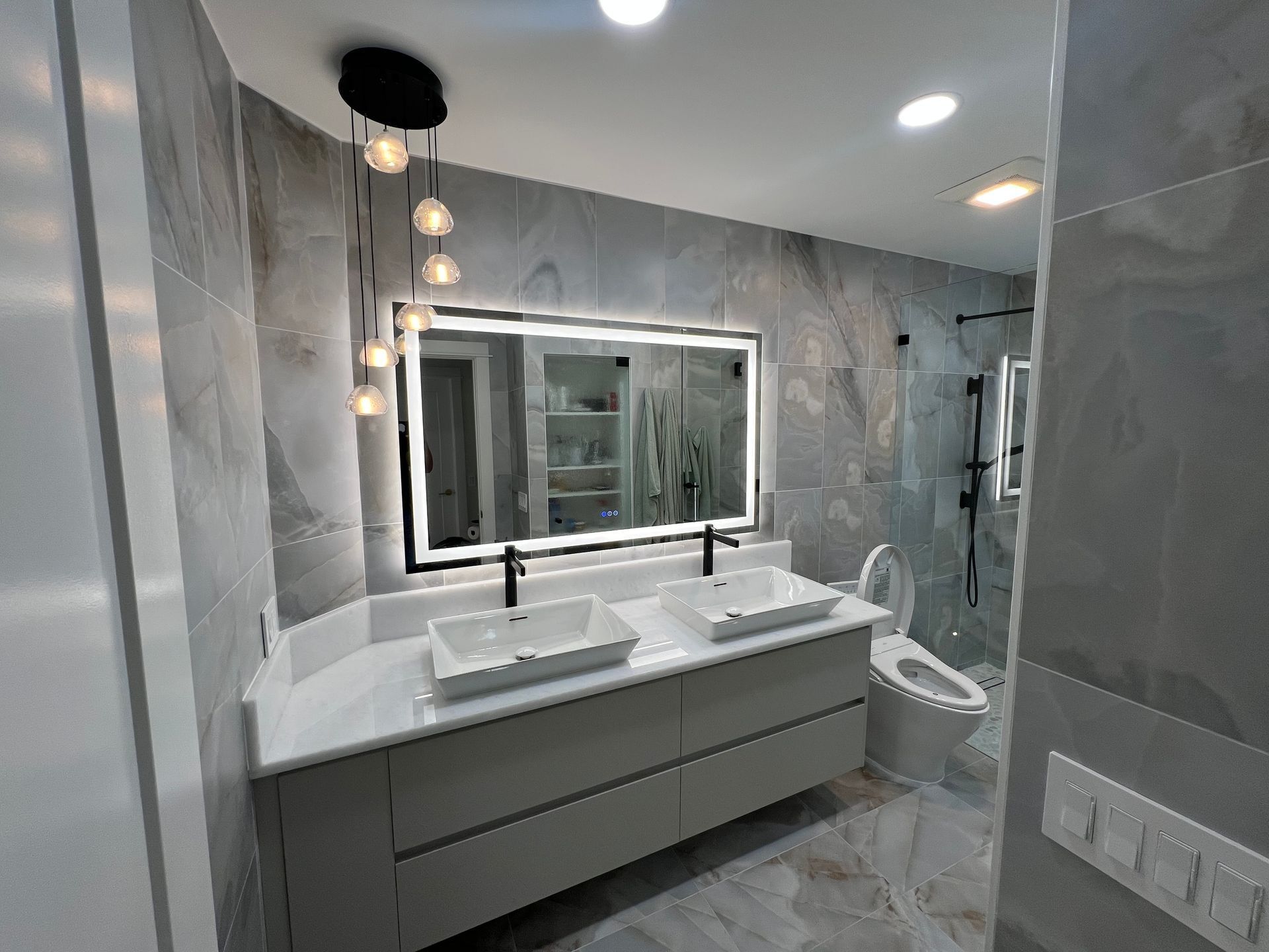 Modern gray bathroom with double vanity, round mirror lights, and a shower.