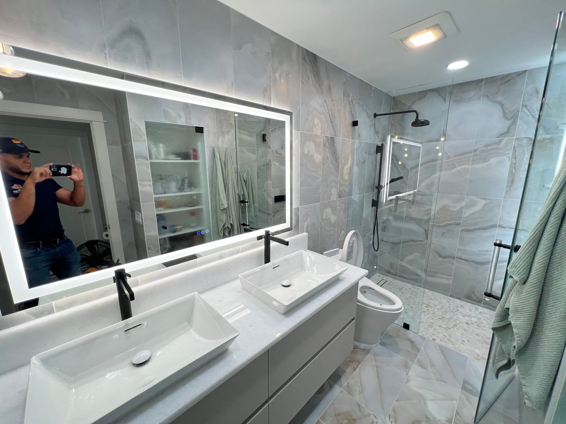 Modern bathroom with double vanity, large mirror, shower, and gray marble walls