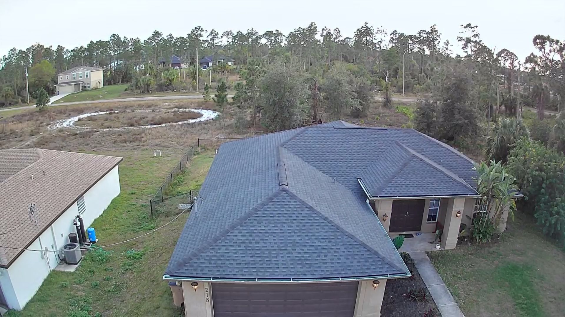 Aerial view of two dark-roofed houses beside a grassy yard and trees in a rural area.