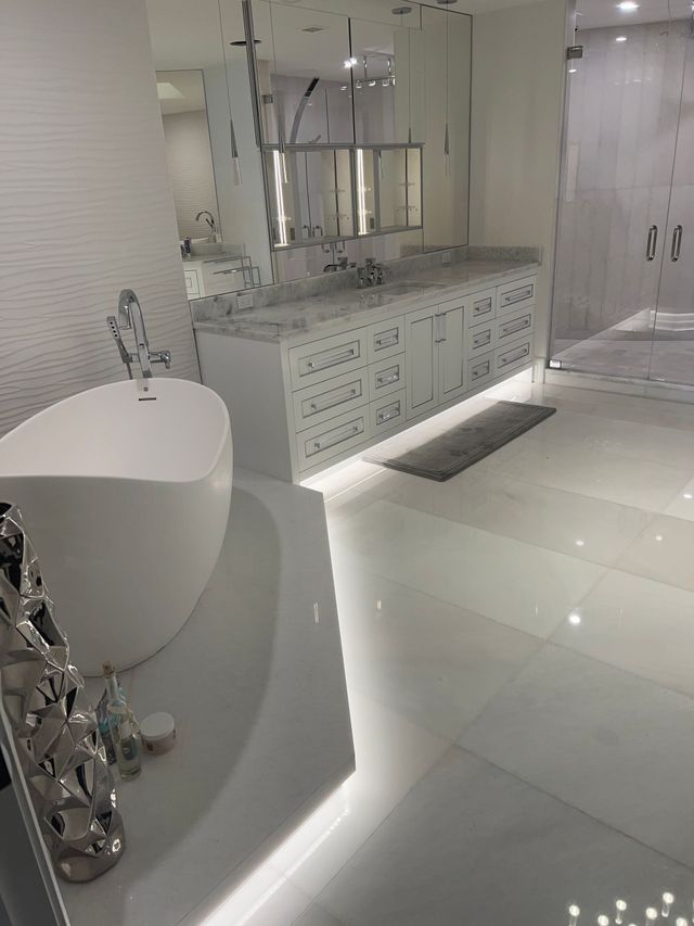 Modern white bathroom with freestanding tub, long vanity, mirrors, and large glass shower enclosure