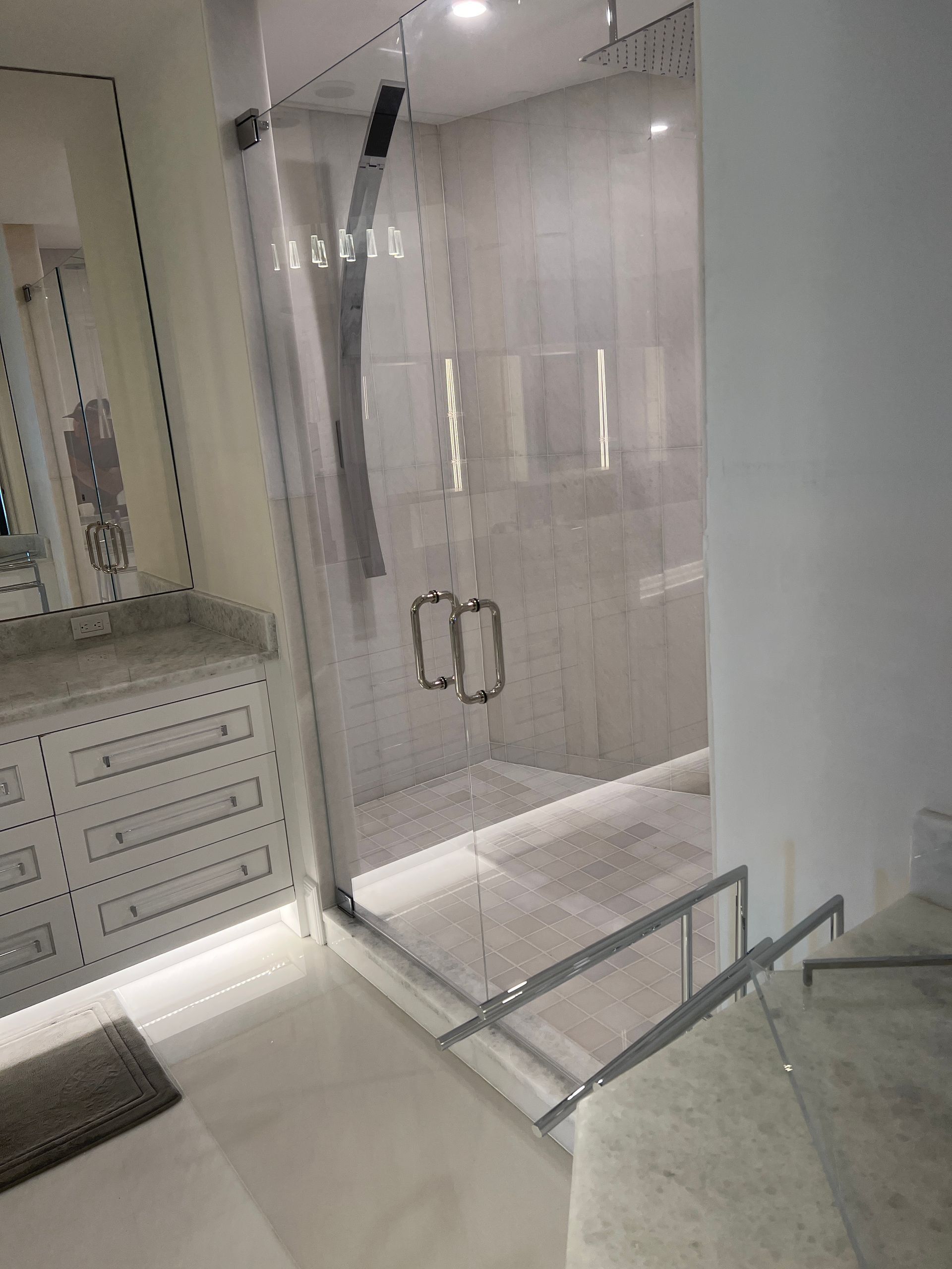 Bathroom with glass shower enclosure, white vanity cabinets, and marble countertop.
