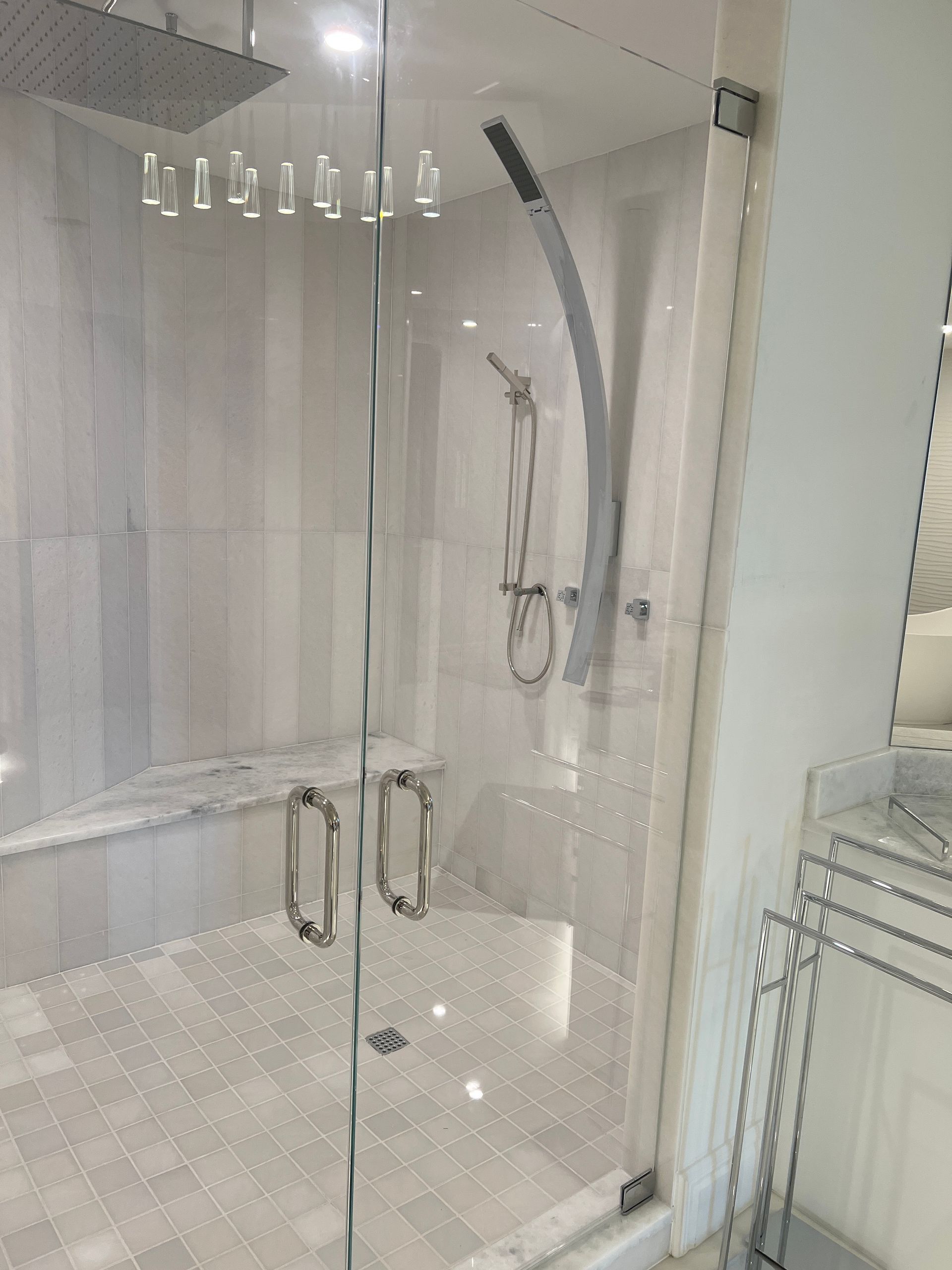 Glass shower enclosure with chrome handles and a handheld shower in a white tiled bathroom