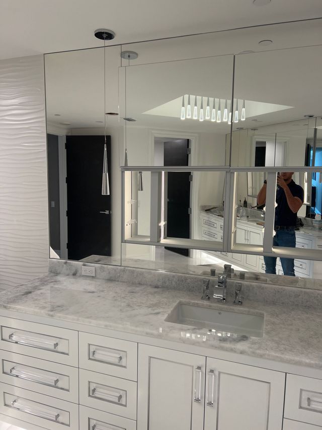 Bathroom vanity with marble countertop, mirror cabinets, and a person taking a mirror selfie in the reflection