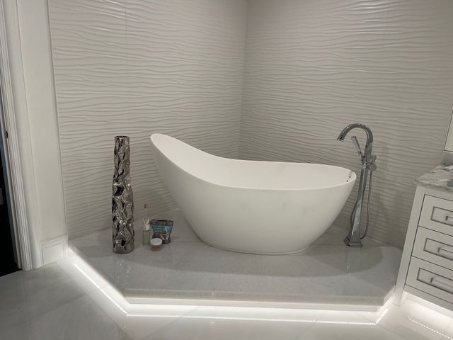 Modern white bathroom vanity with sculptural sink, chrome faucet, and textured wall tiles