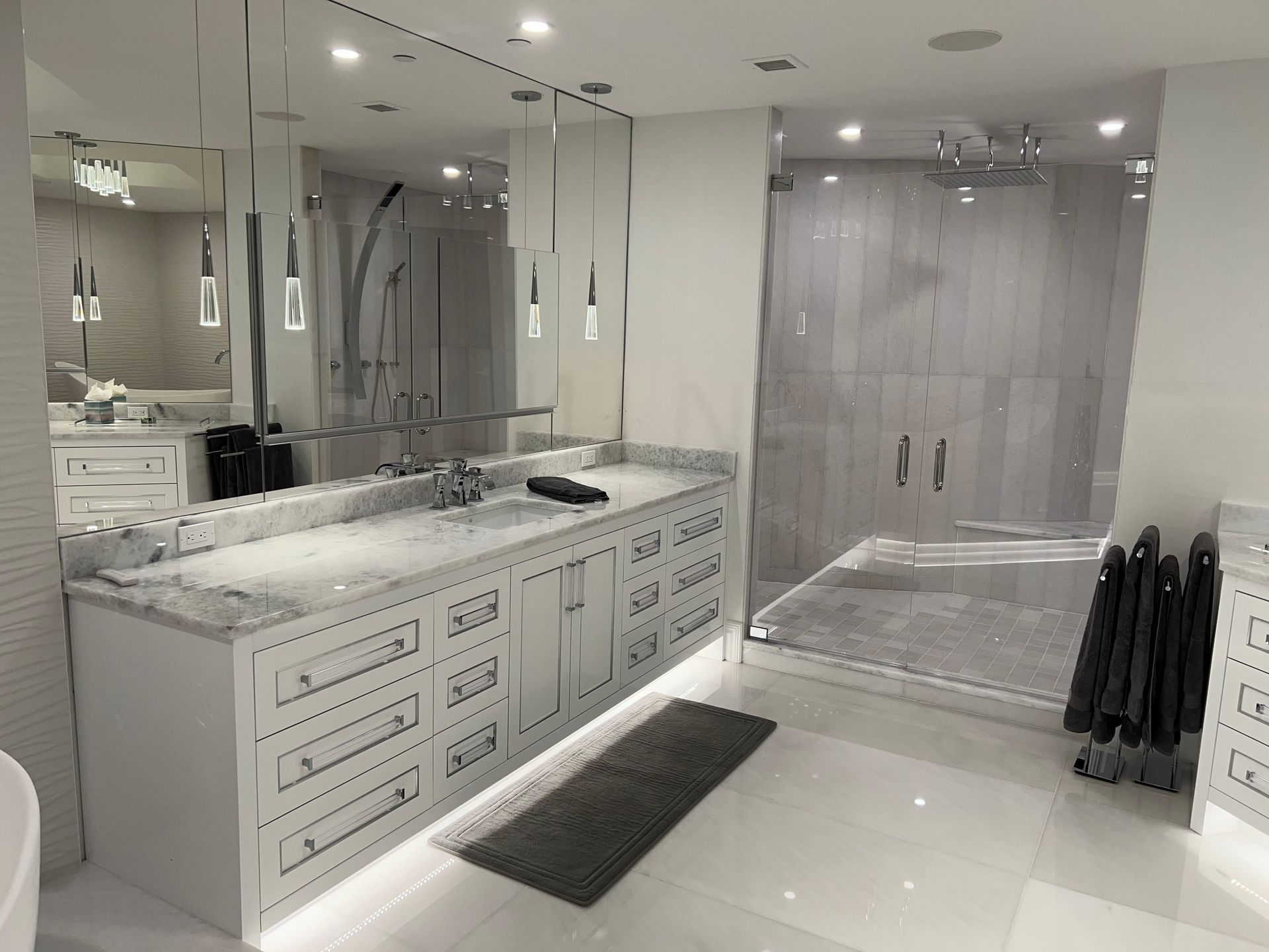 Modern bathroom with double vanity, large mirror, glass shower, and white marble finishes