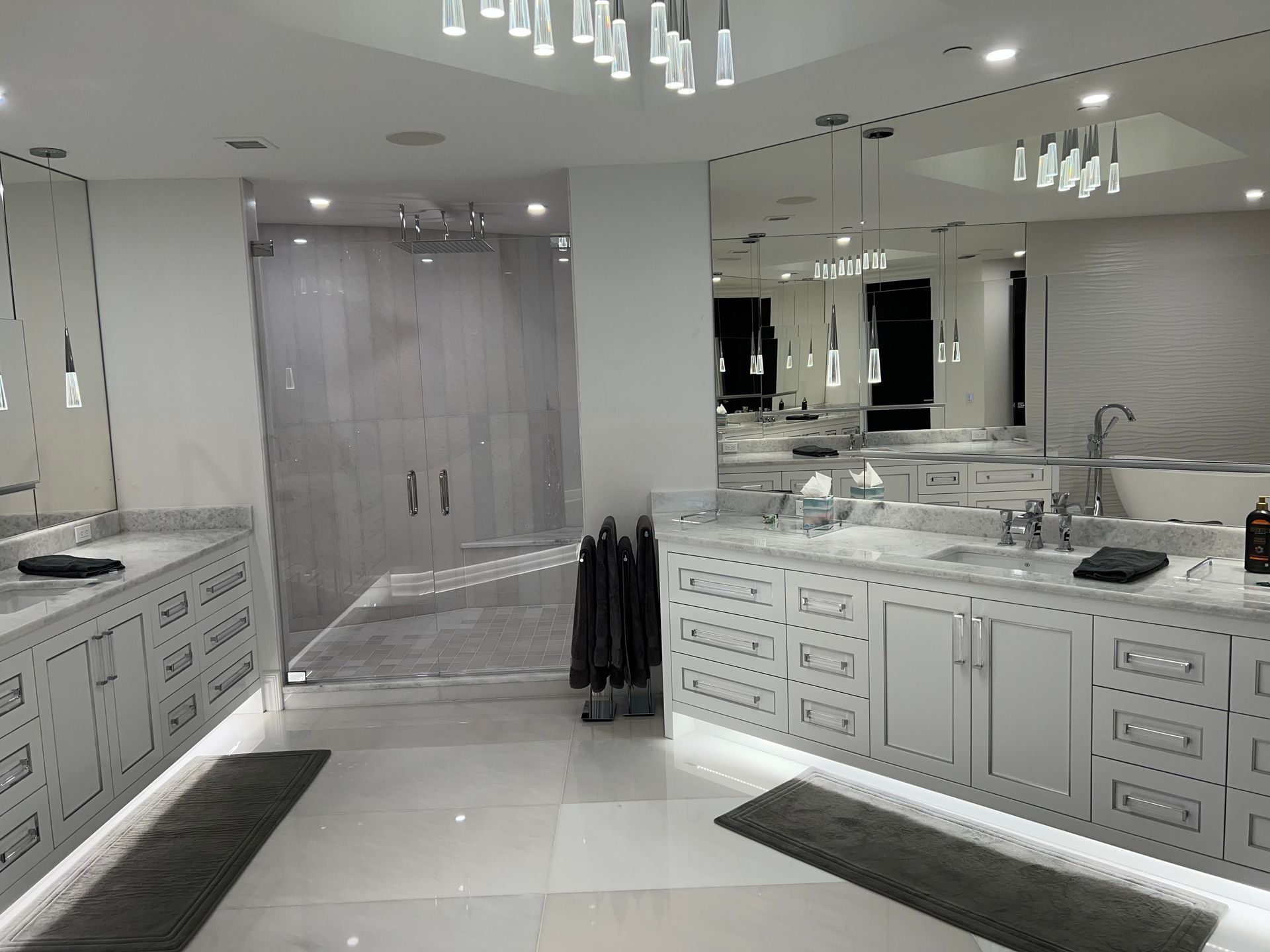 Spacious modern bathroom with double sinks, large mirrors, white cabinetry, and gray tile flooring.