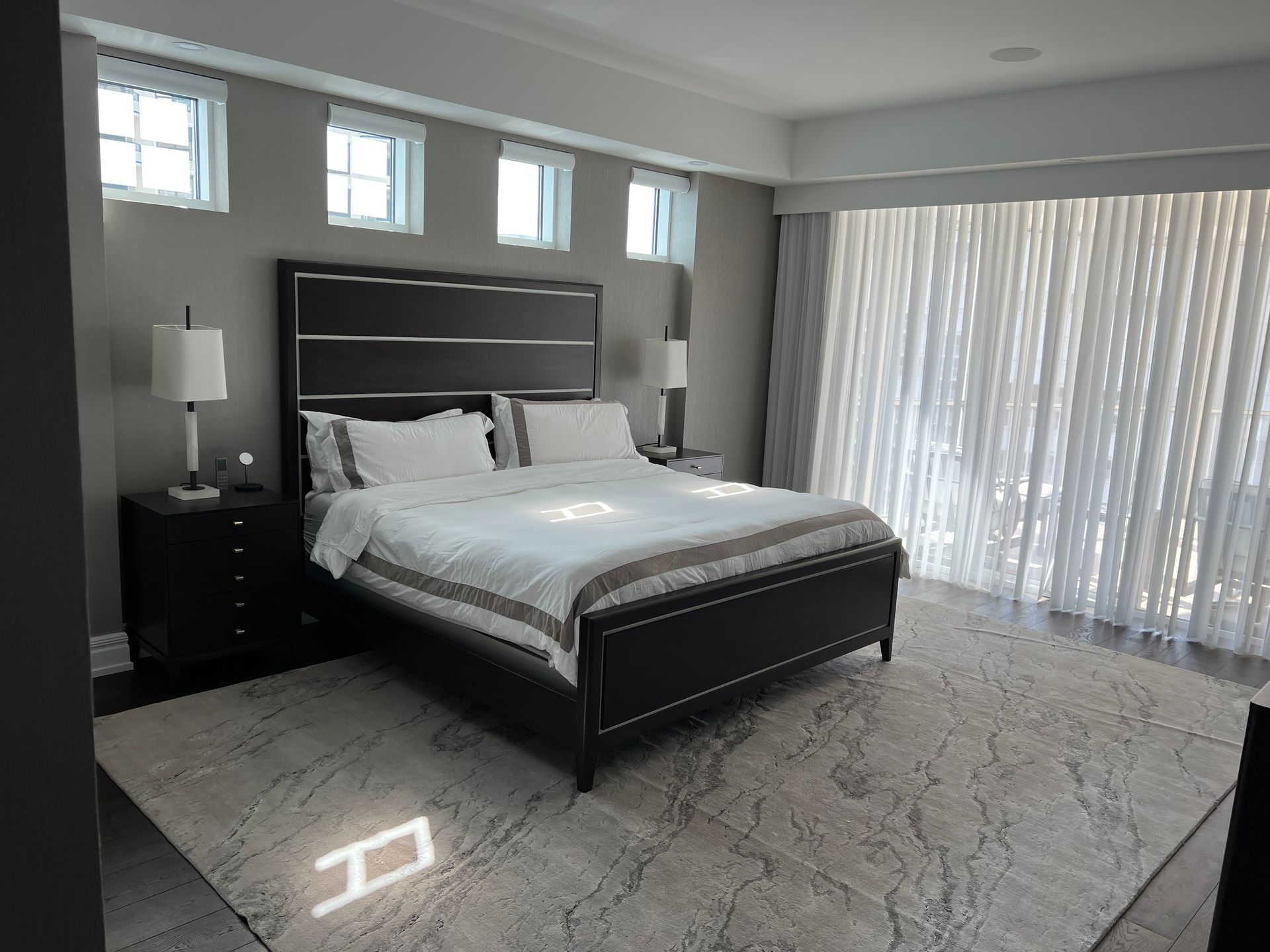 Modern bedroom with a dark wood bed, white bedding, nightstands, and sliding glass doors with sheer curtains