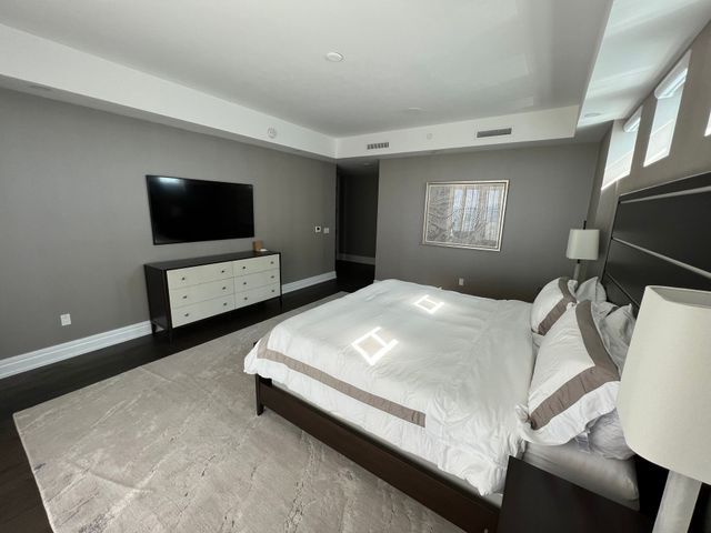 Modern bedroom with king bed, TV on dresser, gray walls, and large windows