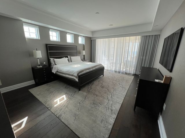 Spacious modern bedroom with a king bed, gray rug, dark wood dresser, and sheer curtains over sliding glass doors