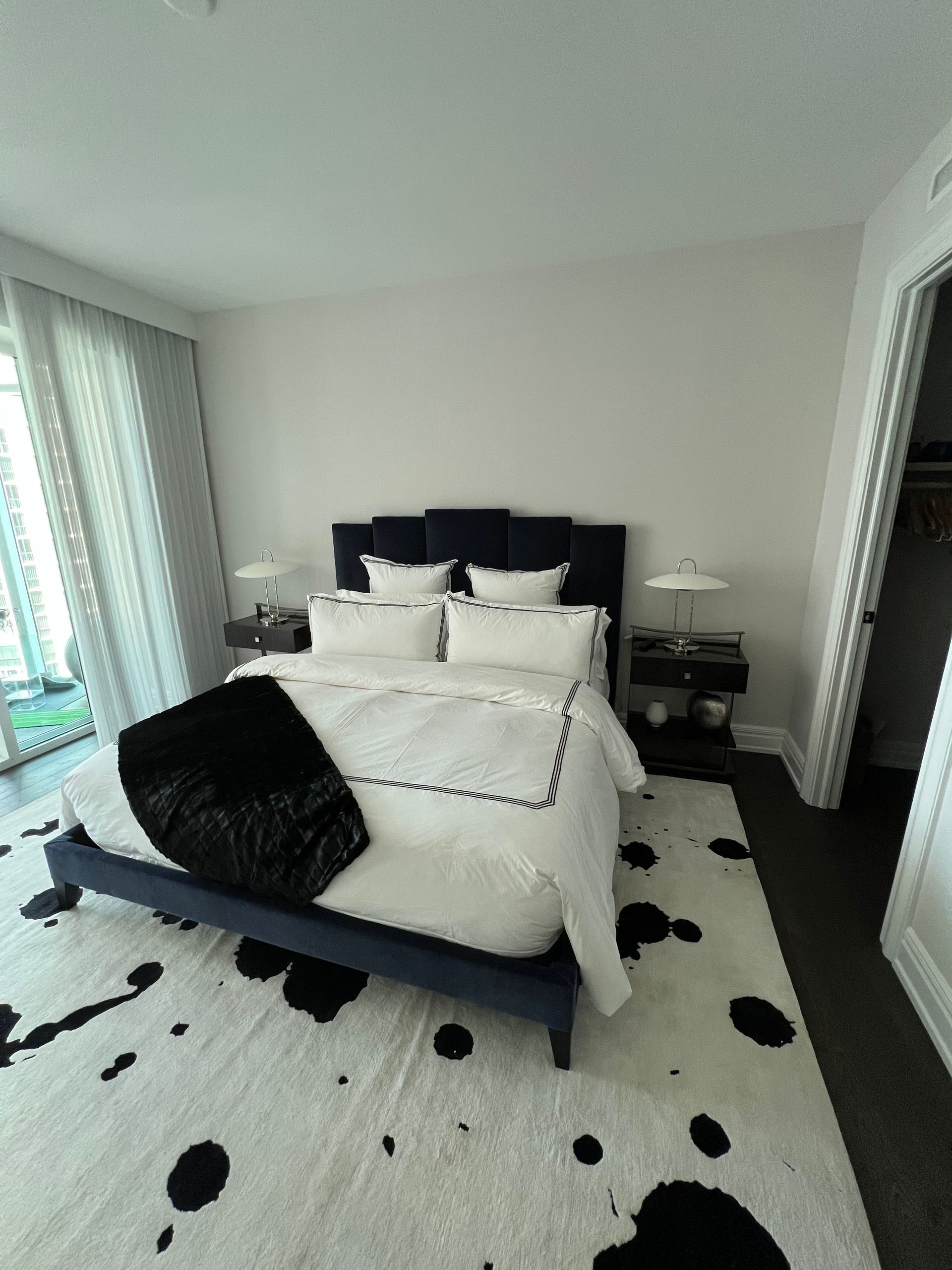 Bright bedroom with a made bed, black pillows, and a black-and-white rug, viewed from the doorway