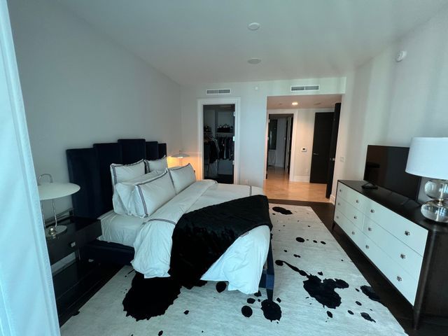 Modern bedroom with a black-and-white bedspread, dresser, lamps, and open closet doorway