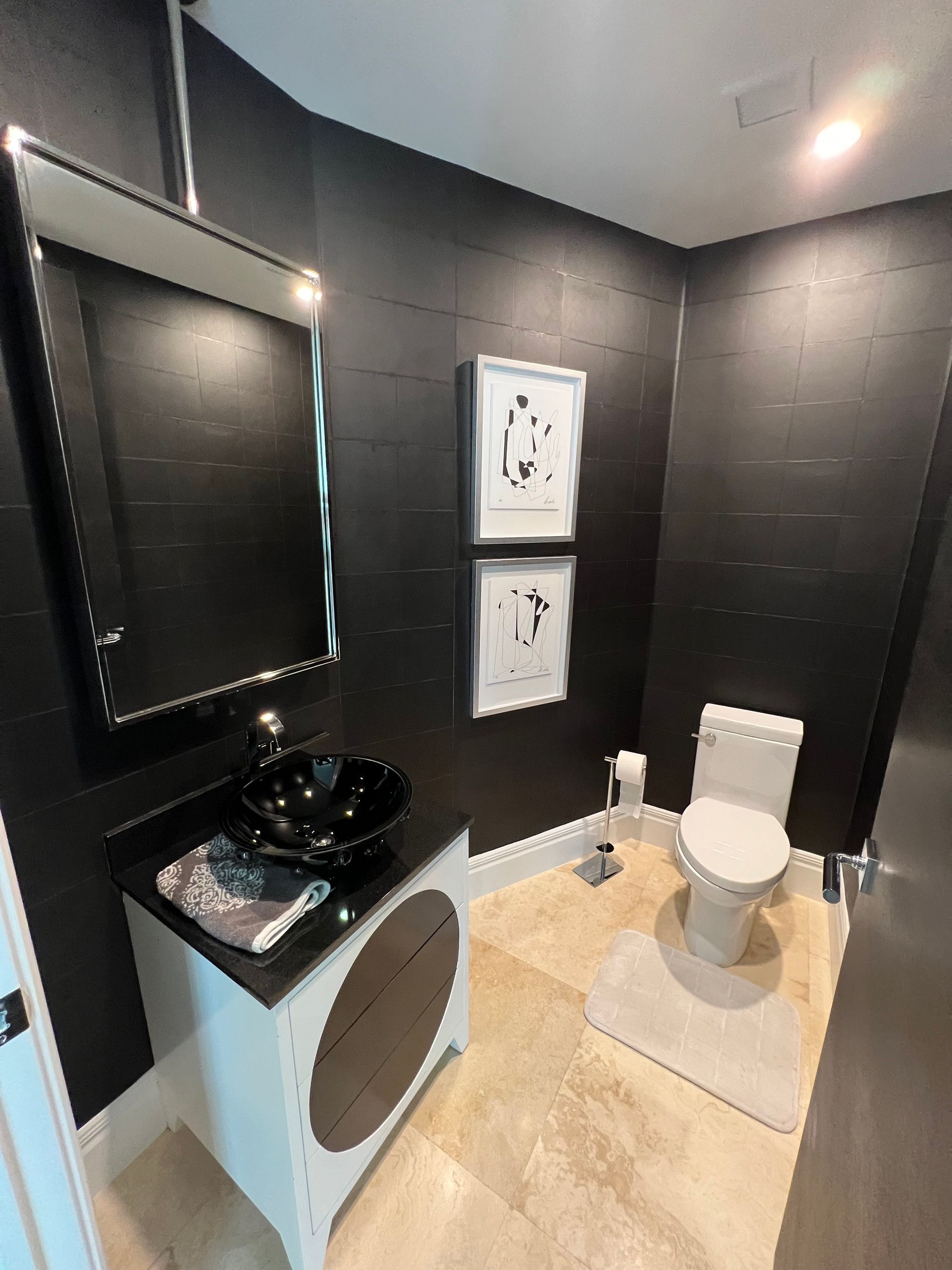 Modern black-and-white restroom with a toilet, sink, mirror, and framed wall art