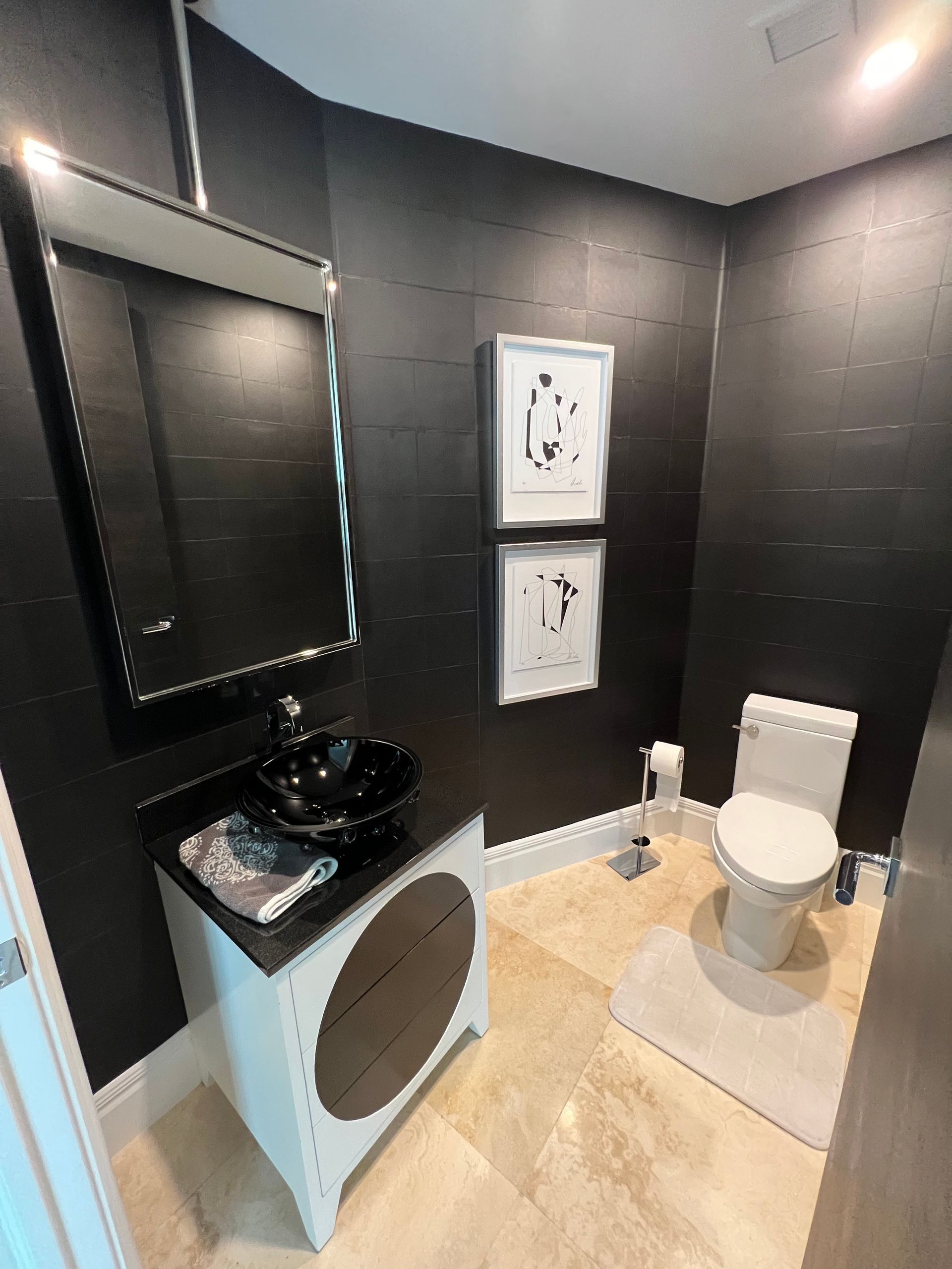Modern black-and-white bathroom with a toilet, sink, mirror, and framed wall art.