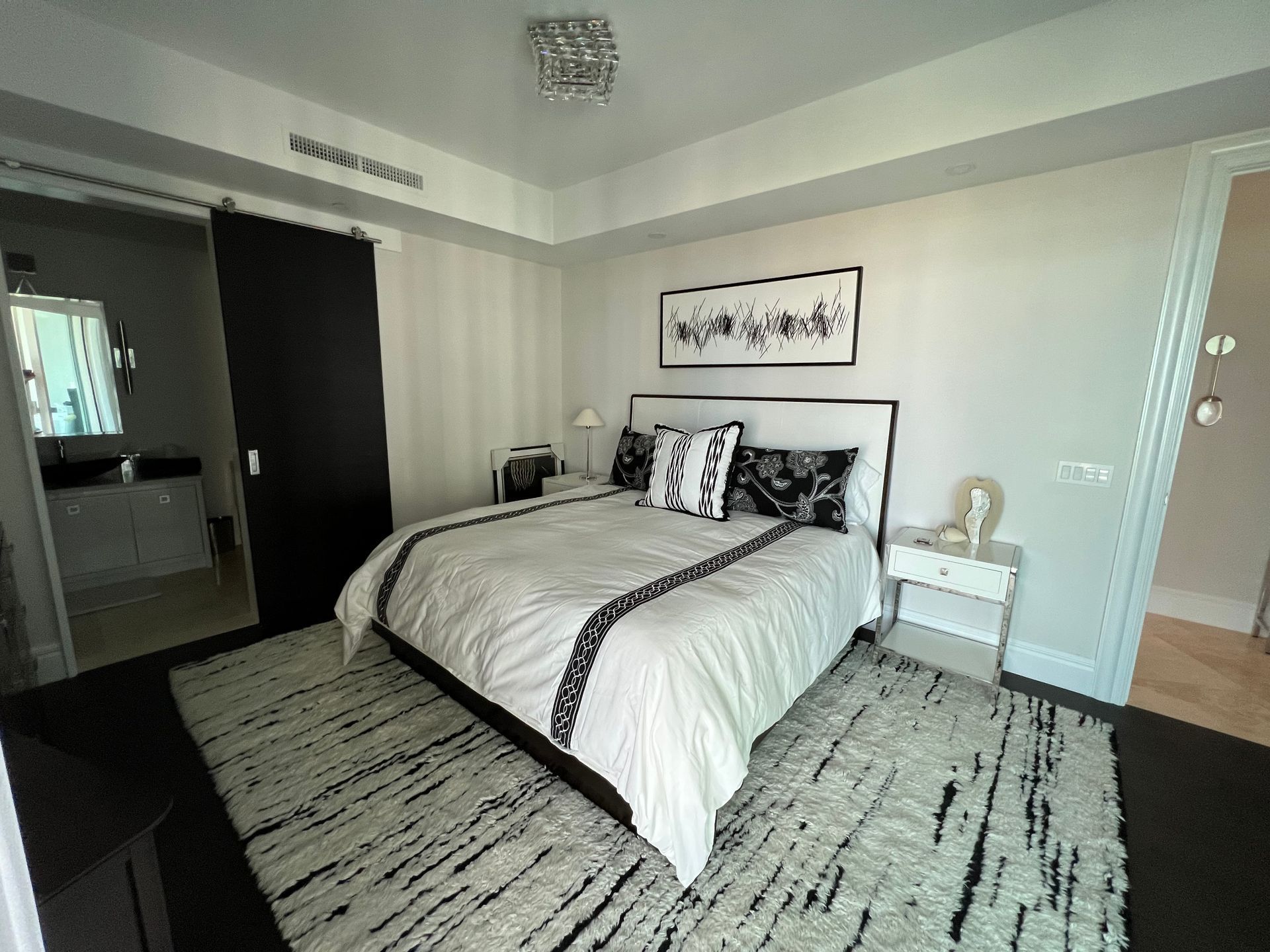 Bright modern bedroom with a bed, patterned rug, nightstands, and framed wall art