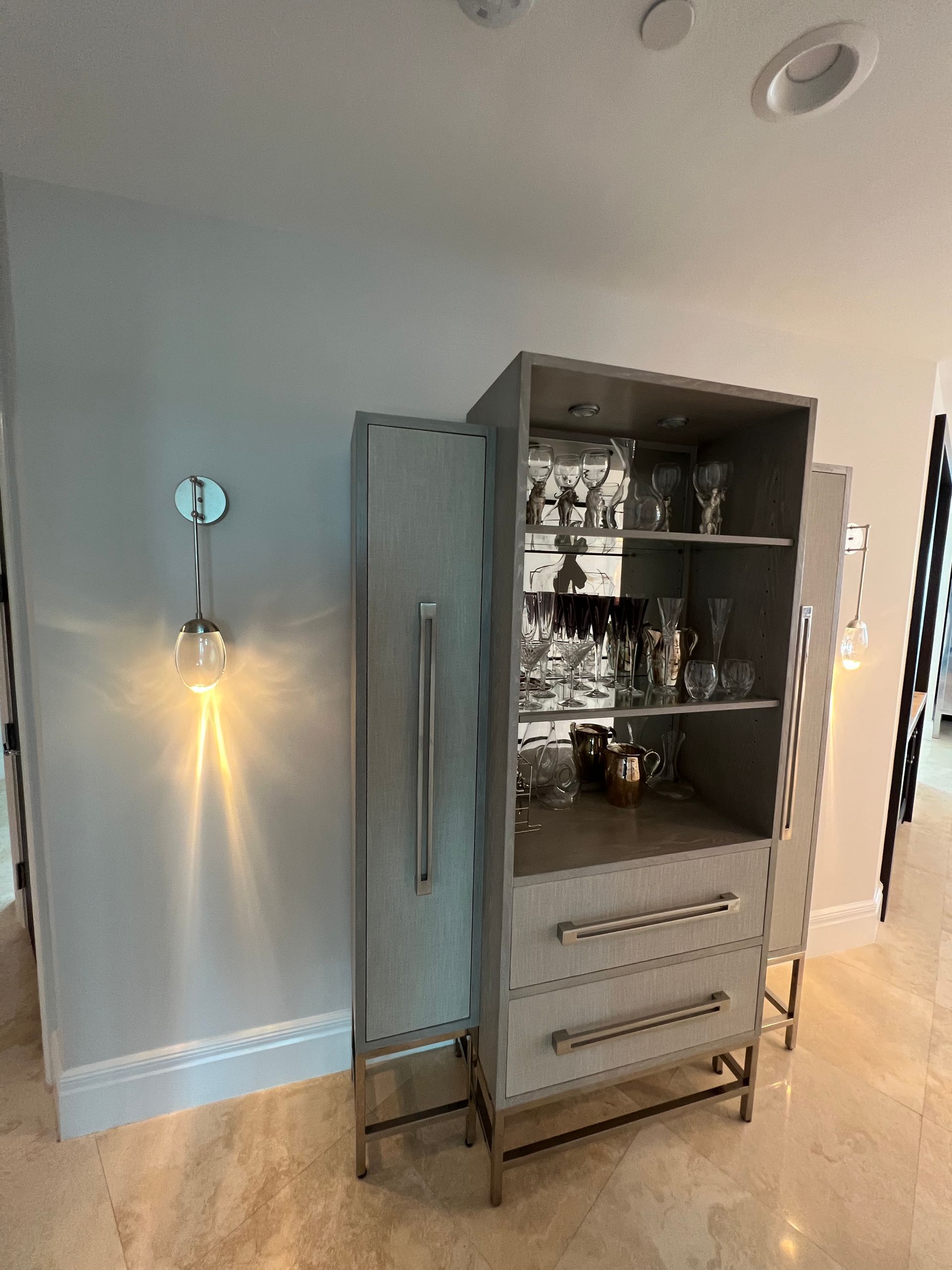 Open cabinet with dishes and drawers in a light blue room, next to a wall sconce and mirror