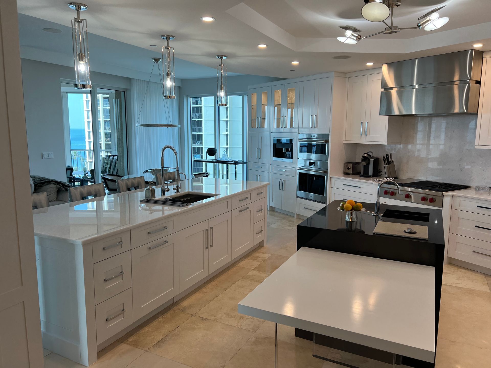 Modern white kitchen with island, stainless steel appliances, pendant lights, and a dining table by the window