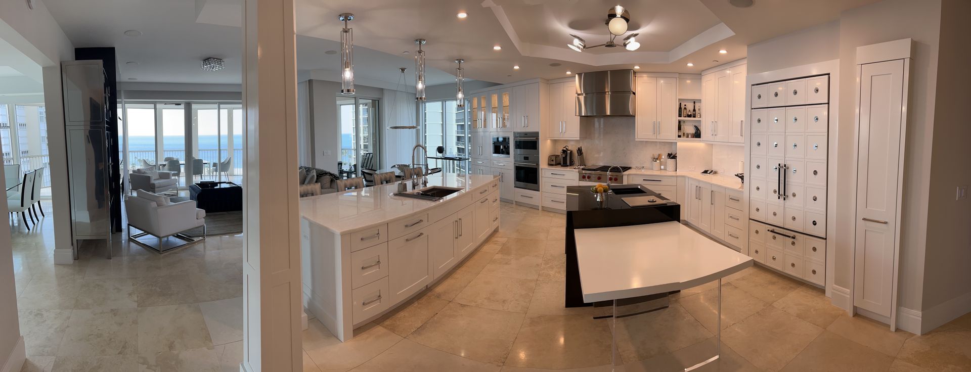 Spacious modern white kitchen with island, marble counters, and open view to a bright living area