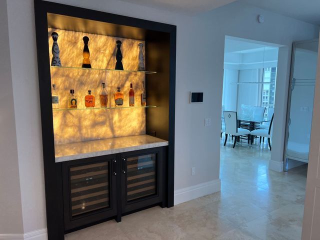 Built-in backlit display cabinet with bottles and decor in a modern hallway near a dining room