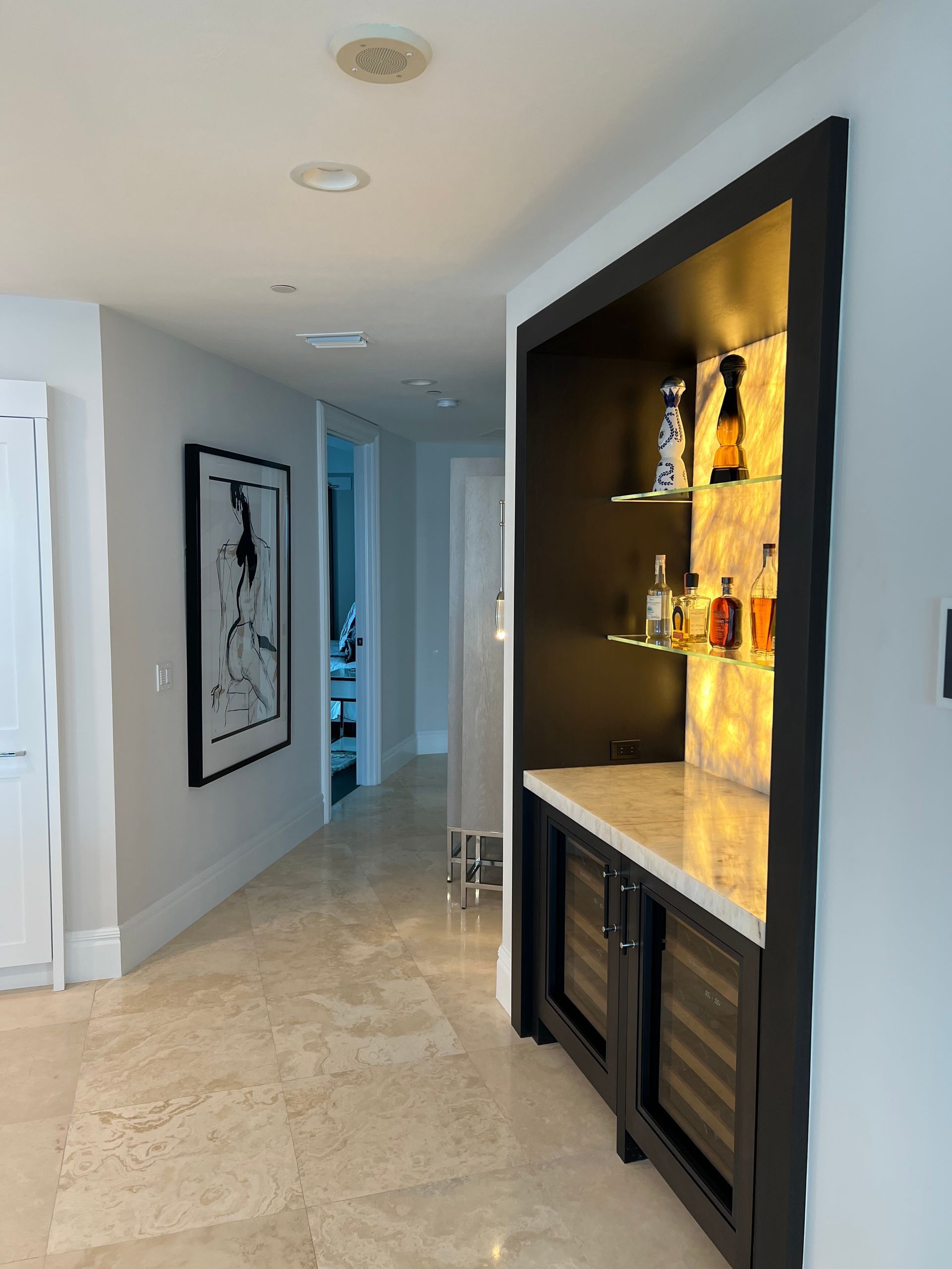 Modern hallway with built-in lit display niche, framed wall art, and beige tile flooring