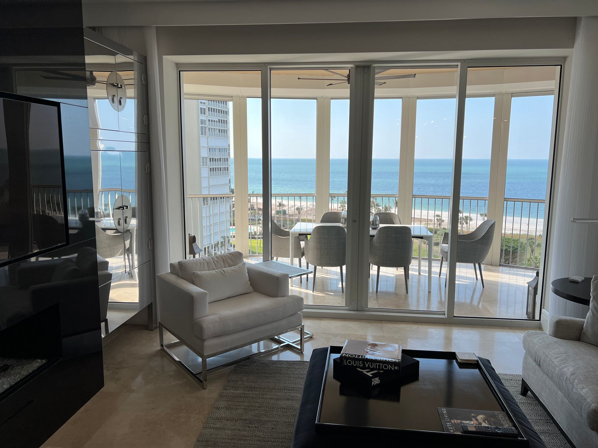 Bright living room with floor-to-ceiling windows overlooking a balcony and ocean view