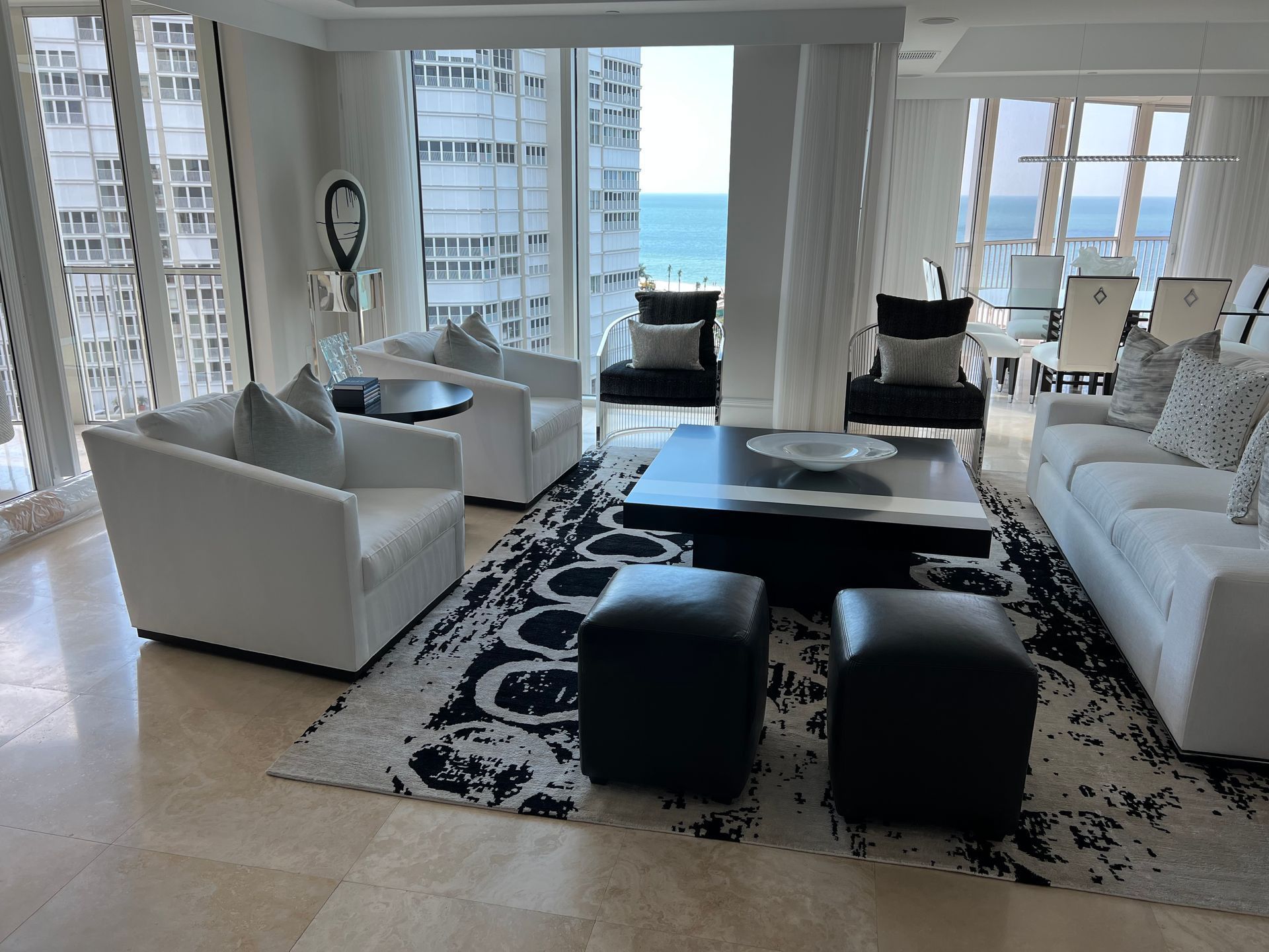 Bright modern living room with white furniture, black ottomans, and ocean view through large windows