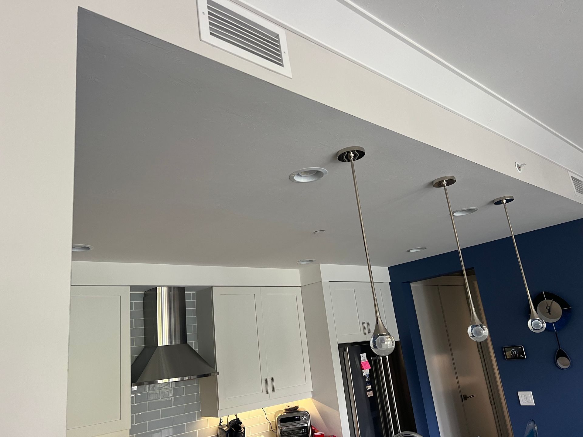 Modern kitchen with blue walls, white cabinets, stainless range hood, and hanging pendant lights