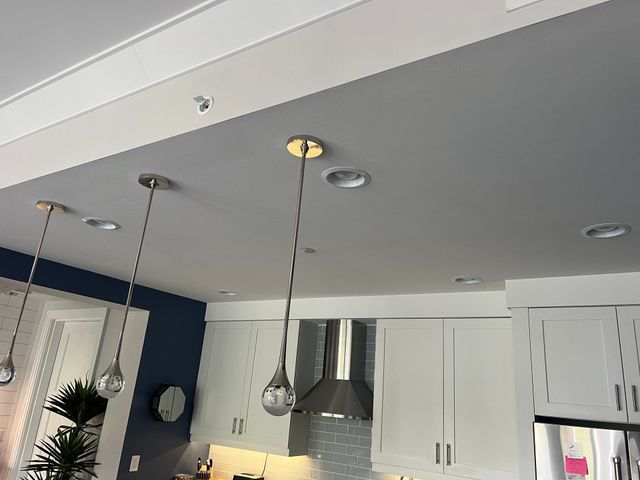 Modern kitchen with white cabinets, stainless range hood, and hanging pendant lights near a blue accent wall