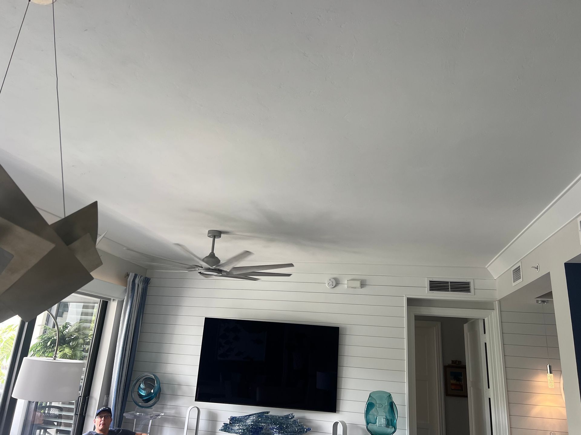Living room with a wall-mounted TV, ceiling fan, white brick accent wall, and large windows
