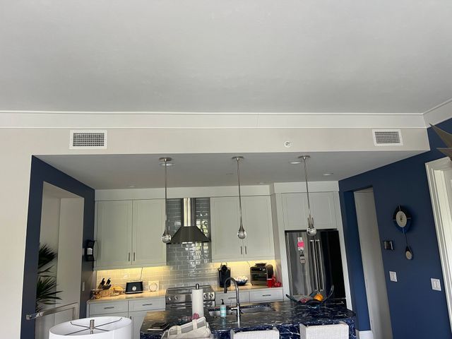 Modern kitchen with white cabinets, blue walls, pendant lights, and a stainless steel refrigerator.