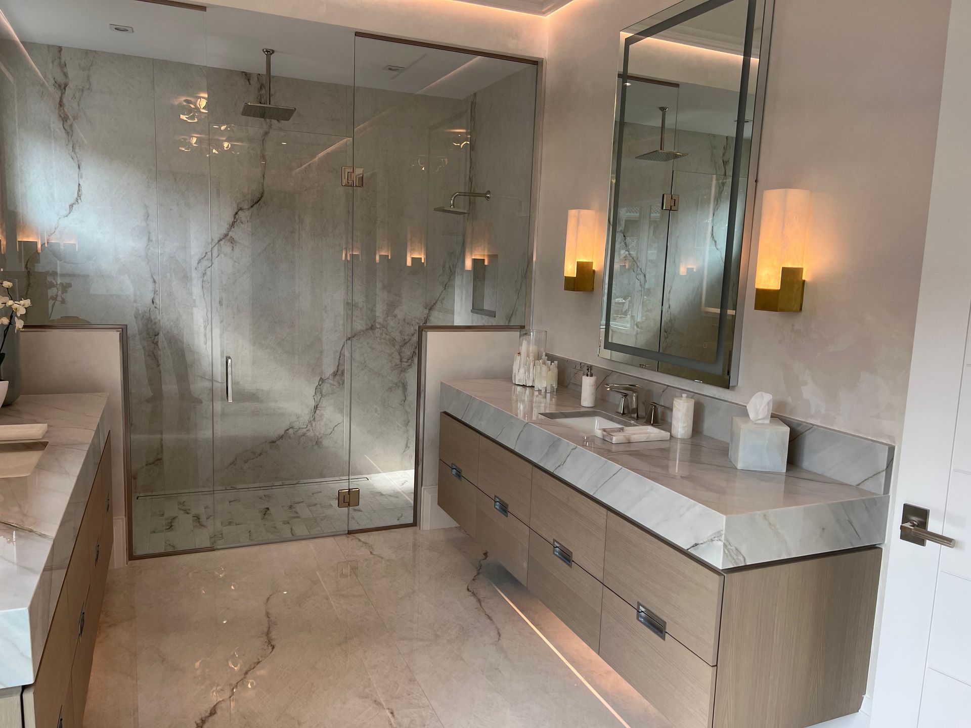 Modern bathroom with double vanity, large mirror, glass shower, and beige marble finishes