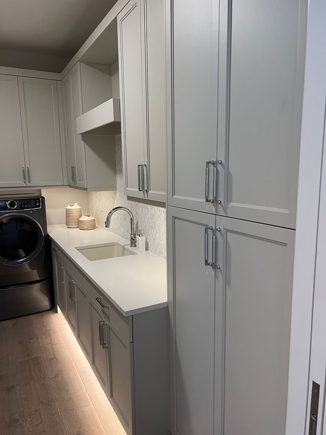 Narrow laundry room with gray cabinets, white countertop, sink, and stacked washer and dryer