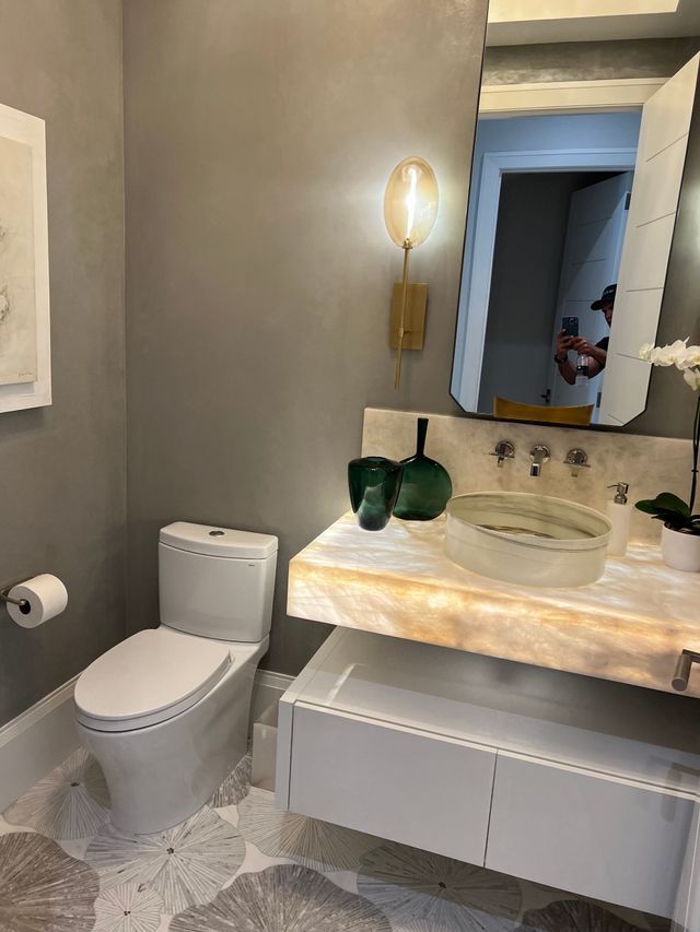 Small modern bathroom with toilet, wall-mounted vanity, mirror, and green vases on the counter.