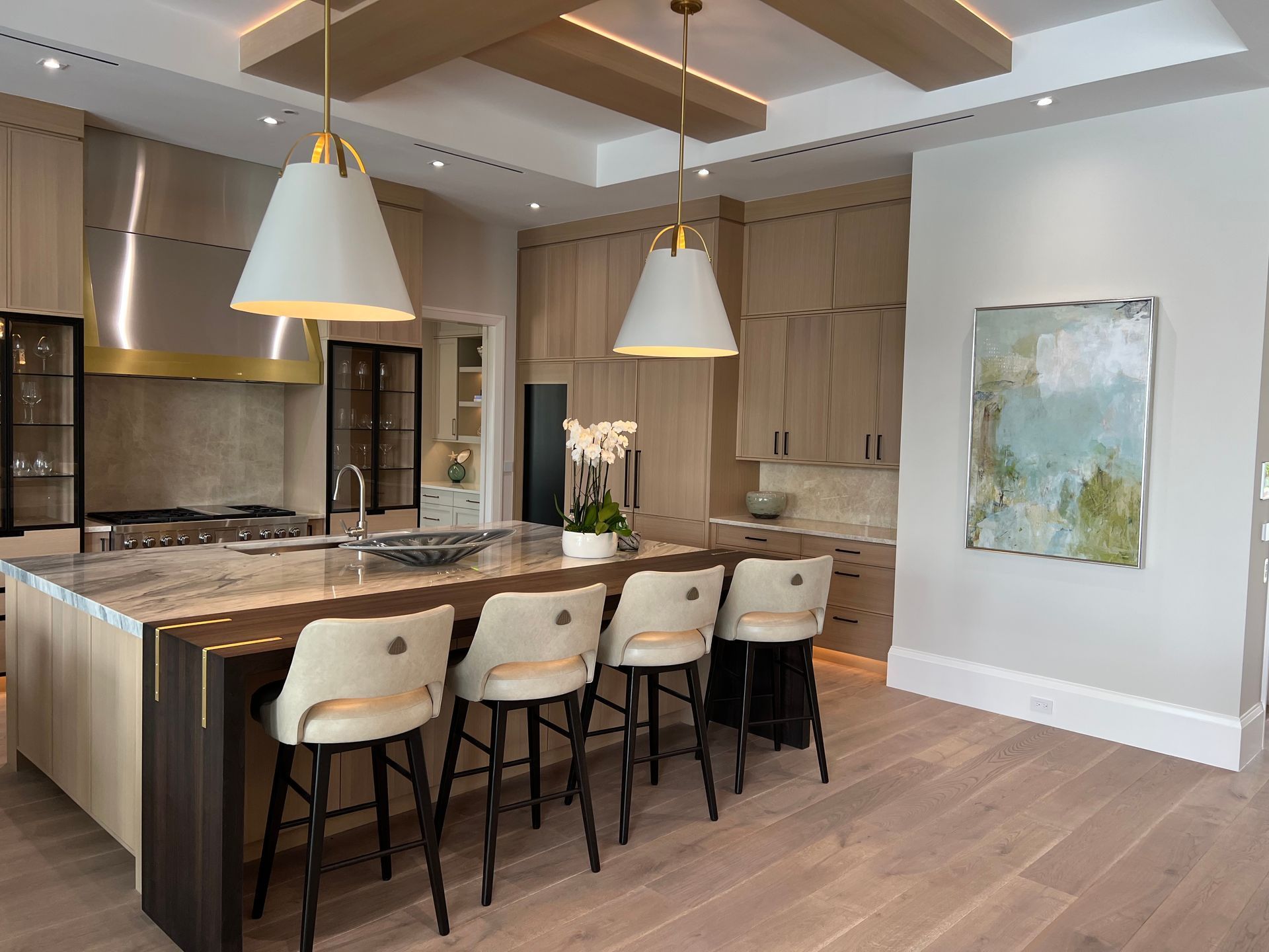 Modern kitchen with wood island, four stools, pendant lights, and a dining nook by an abstract wall painting