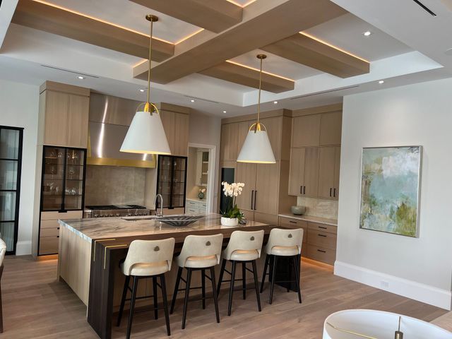 Modern kitchen with large island, pendant lights, bar stools, and wood-accented ceiling панели