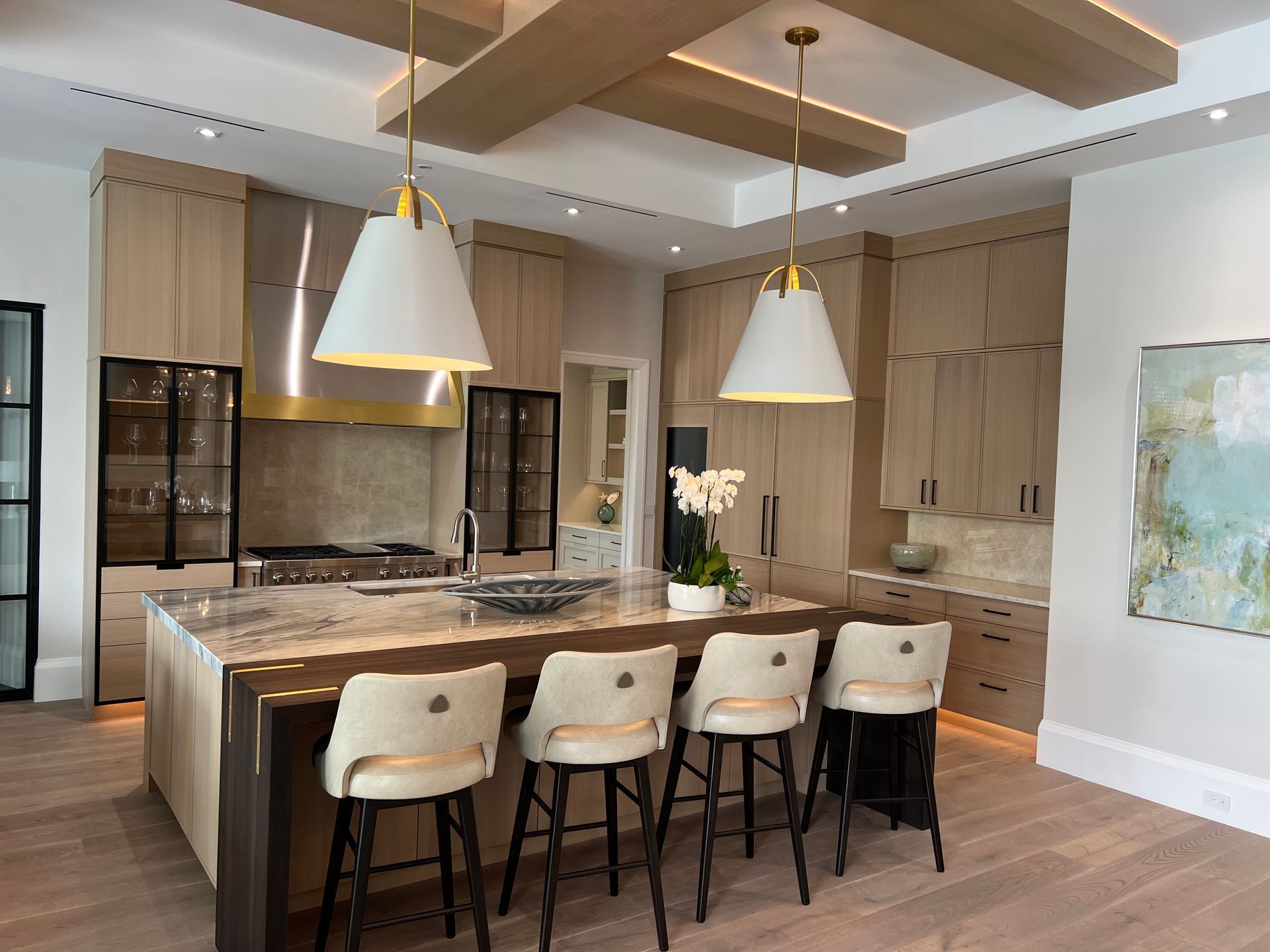 Modern kitchen with a large island, white stools, and pendant lights in a bright open-plan home