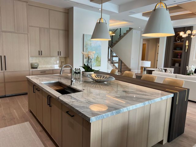 Modern kitchen with large marble island, pendant lights, and light wood cabinetry