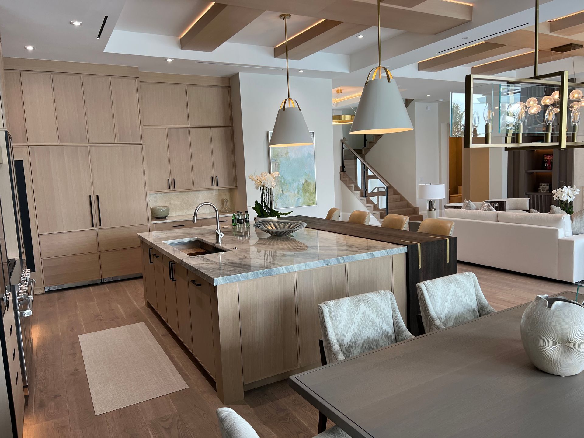 Modern kitchen with large island, wood cabinetry, pendant lights, and an open view to a bright living area