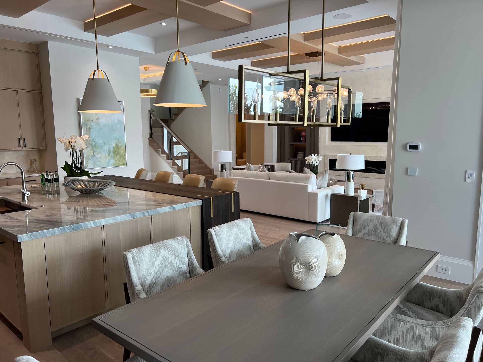 Modern open-plan dining and kitchen area with a gray table, pendant lights, and large windows