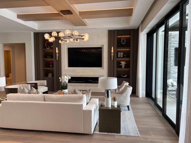 Modern living room with white sofas, wall-mounted TV, chandelier, and floor-to-ceiling windows
