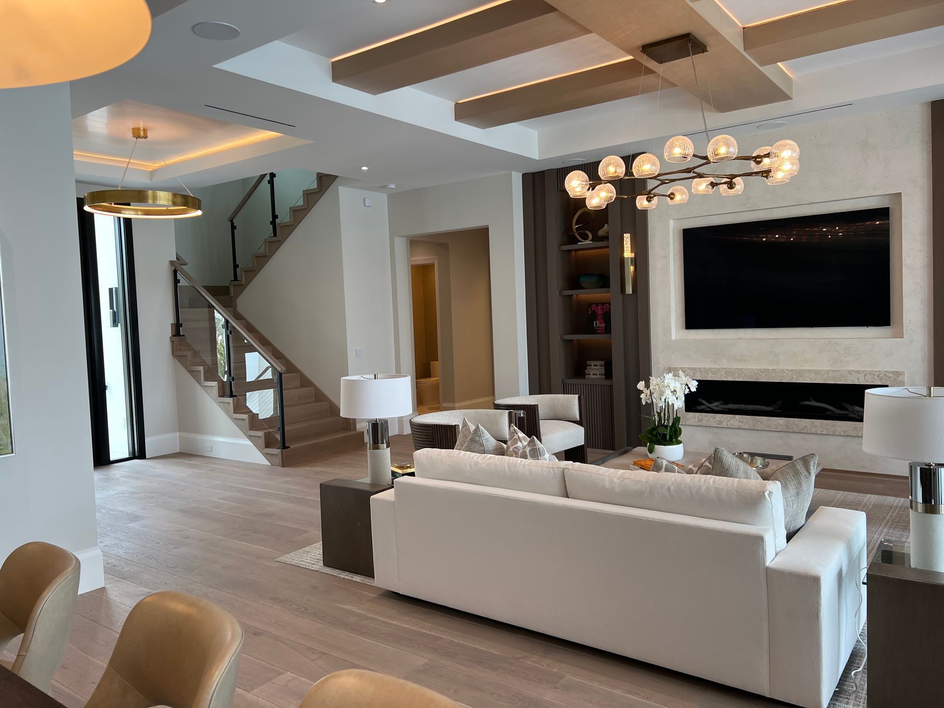 Modern living room with white sofas, TV, staircase, and chandelier lighting