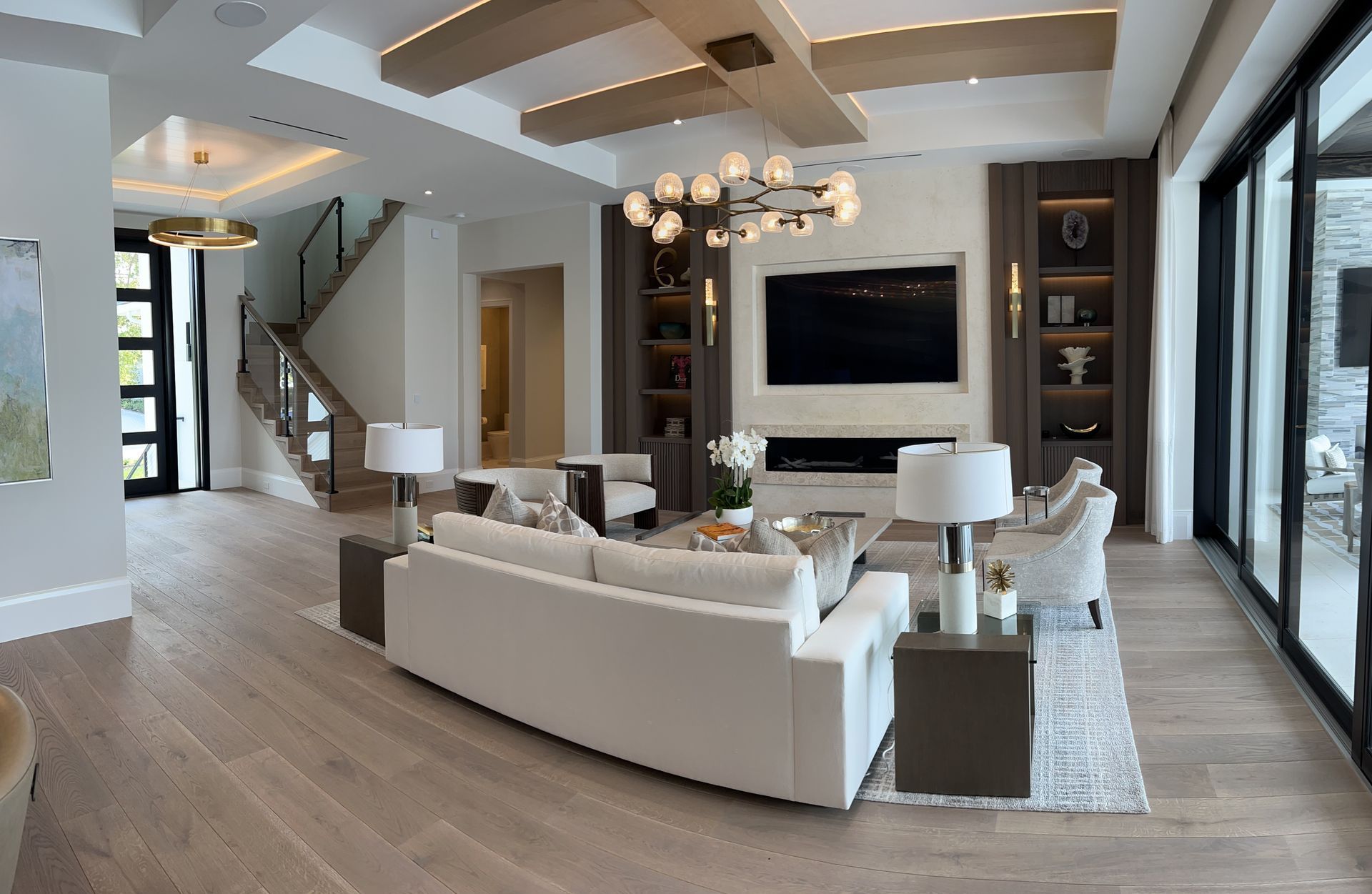 Modern open-concept living room with white sectional, fireplace, staircase, and large windows